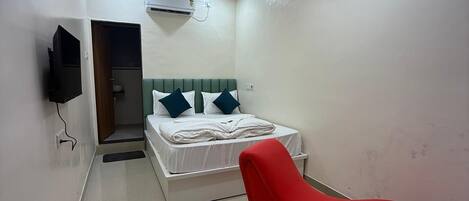 A modern hotel room with a bed, a red chair, a flat-screen TV, and an air conditioning unit.