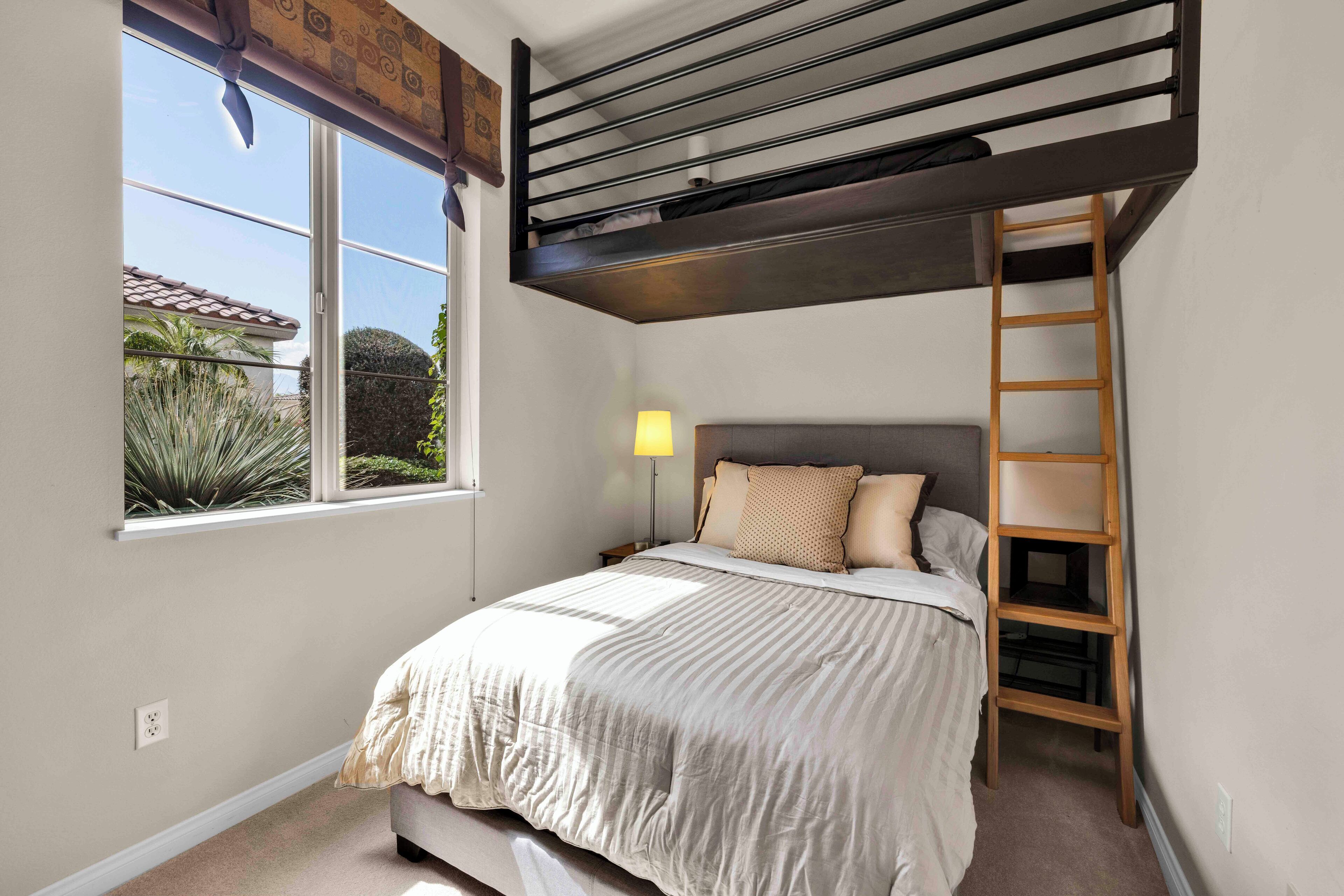 Un dormitorio con literas, una ventana con vistas a la vegetación, una lámpara de noche y una escalera de madera.