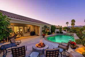 A pool area with a fire pit, lounge chairs, and a patio. - Desert Fairway Oasis (Indio)