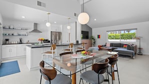 A modern kitchen with white cabinets, a central island, and a dining area with a glass table and chairs. - Kaptur Palms (Palm Springs)