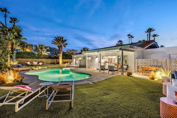 A backyard with a swimming pool, outdoor furniture, and a covered patio area.