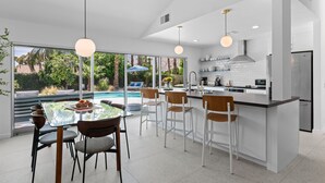 A modern kitchen with a large island, white cabinetry, and a view of a swimming pool. - Kaptur Palms (Palm Springs)
