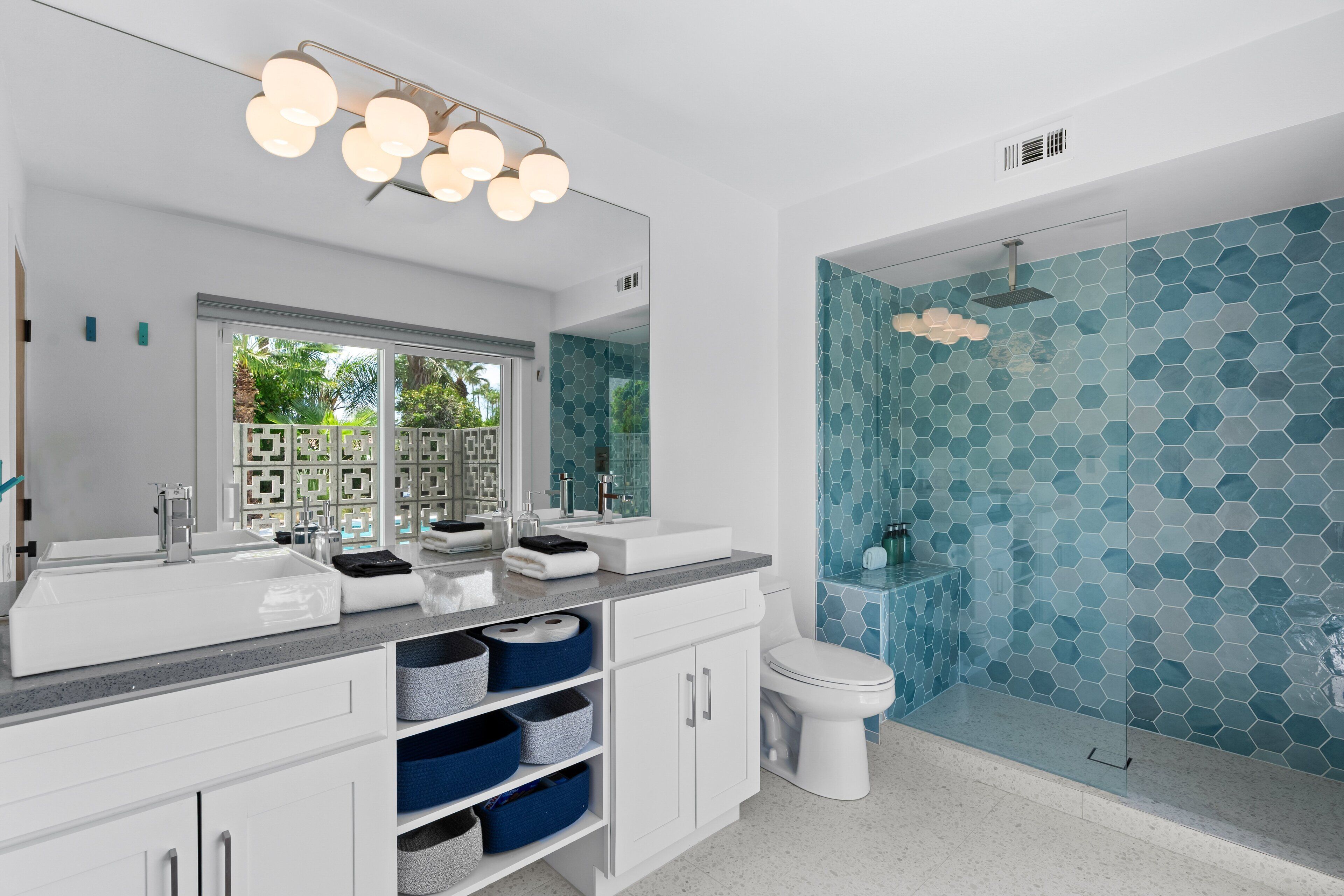 Une salle de bain moderne avec un grand miroir, deux lavabos, des toilettes et une douche à parois de verre.