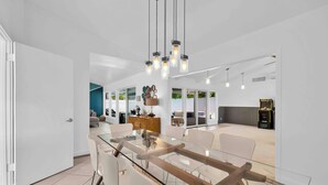 A modern dining area with a glass-top table, white chairs, and pendant lighting.