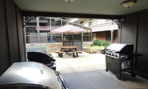 Une terrasse extérieure avec un barbecue, une table avec un parasol et un bac à fleurs en pierre.