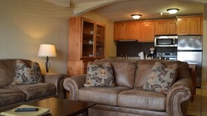 A living room with a brown leather sofa set, a wooden cabinet, and a kitchen area with stainless steel appliances. - 2-bedroom condo in beautiful Park City just in time for Sundance (Park City)