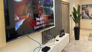 A flat-screen TV mounted on a wall, with a decorative light fixture above it. - Uloobi Apartment  (Abuja)
