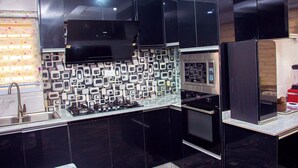 A modern kitchen with black cabinets, a stainless steel range hood, and a patterned backsplash. - Uloobi Apartment  (Abuja)