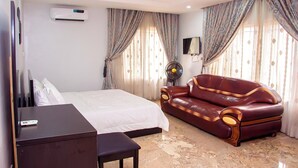 A hotel room with a bed, a leather sofa, a desk, and a TV. - Uloobi Apartment  (Abuja)