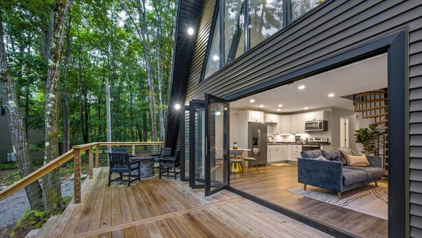 A modern house with a wooden deck, a kitchen, and a living area with a sofa and chairs. - Wanderlust A Frame - Lake/ Beach/ Golf/ Pool/ Trails in Alpine Lake (Terra Alta)