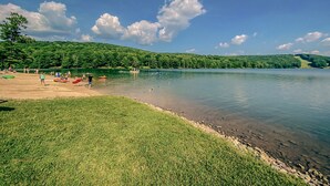 A lakeside scene with a grassy area, a sandy beach, and a calm lake. - Wanderlust A Frame - Lake/ Beach/ Golf/ Pool/ Trails in Alpine Lake (Terra Alta)
