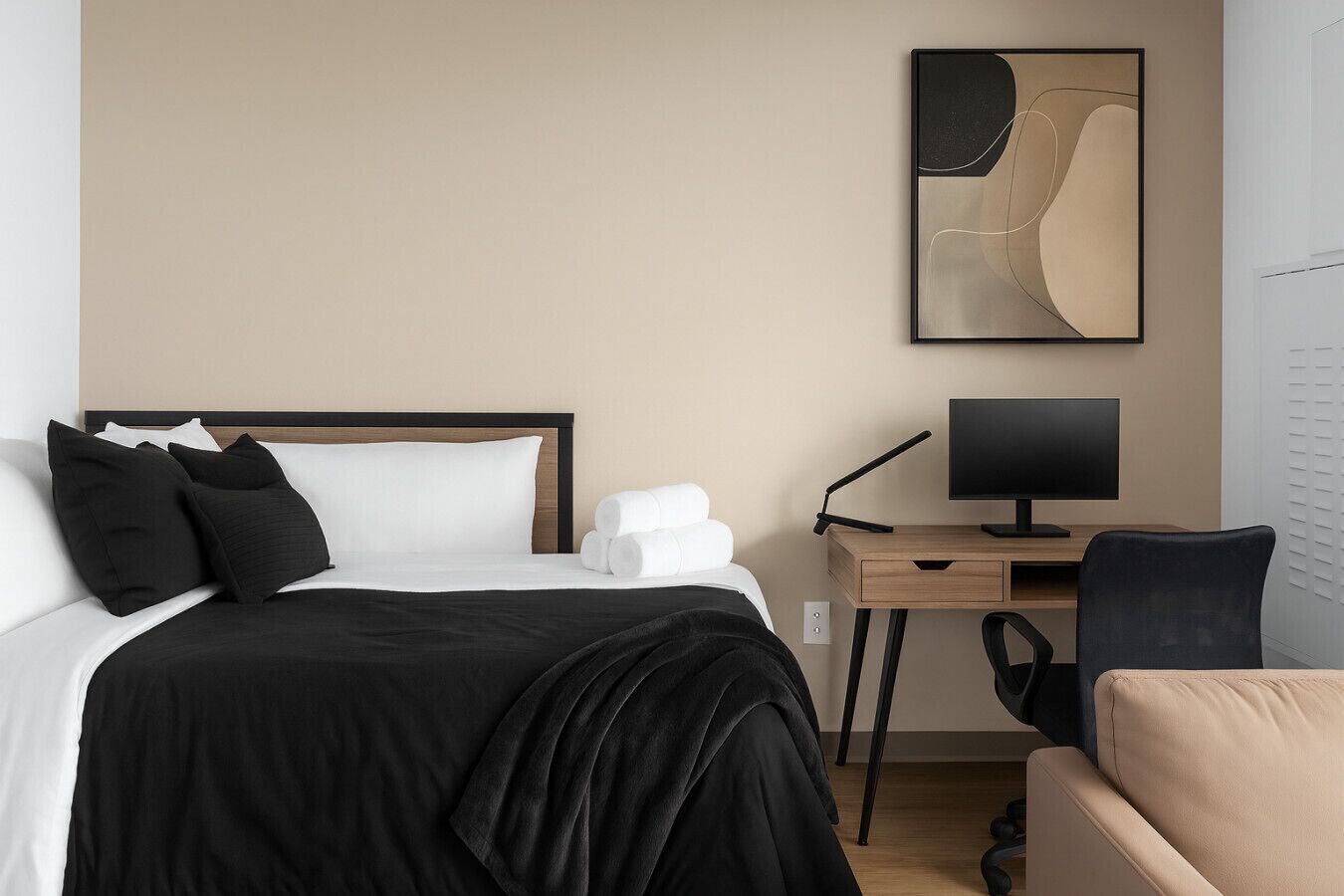 A hotel room with a bed, a desk with a computer, a chair, and a wall-mounted TV.