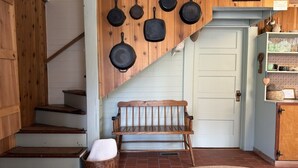 A wooden staircase, a bench, a wall-mounted pan collection, and a white door. - Heart Pine Lodge: 1908 Historic Cozy Cabin Sleeps 8 with Firepit, Pets Welcome (Clayton)