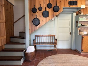 Un escalier en bois, un banc, une collection de poêles accrochée au mur et une porte blanche.