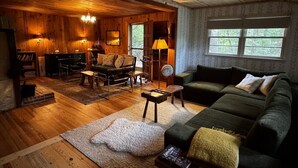 A cozy cabin interior with a wooden floor, a green sofa, a fireplace, and a ceiling fan. - Heart Pine Lodge: 1908 Historic Cozy Cabin Sleeps 8 with Firepit, Pets Welcome (Clayton)