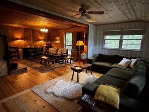 A cozy cabin interior with a wooden floor, a green sofa, a fireplace, and a ceiling fan.