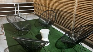 Eine Dachterrasse mit vier schwarzen Gestellstühlen und einem weißen Tisch, umgeben von einem grünen Kunstturfbelag und einem Bambuszaun.