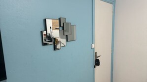 Ein Flur mit blauer Wand und weißer Tür. An der Wand hängt ein Spiegel und eine kleine Ablage mit einer Tasse und einem Buch.