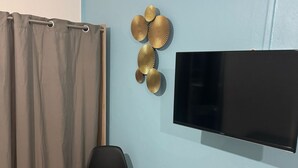 Ein Zimmer mit Glastisch, schwarzem Stuhl, Wandfernseher und Vorhang.