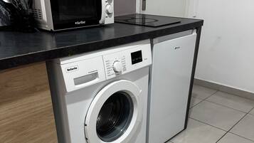 A compact washer and dryer unit with a control panel, placed on a tiled floor with a wooden cabinet adjacent to it.