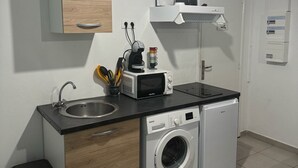 Eine kompakte Küche mit Spüle, Mikrowelle und Waschmaschine, einem Holzkorpus und einer Pendelleuchte.