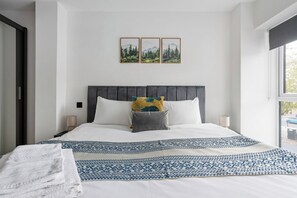 A bedroom with a bed, pillows, a patterned bedspread, a window, and three framed pictures on the wall.
