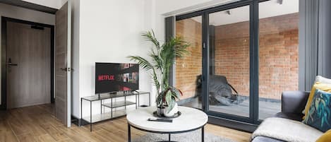 En moderne stue med et fladskærms-tv, et rundt sofabord, en sofa og en stor skydedør med glas, der fører ud til en murstensfacade.