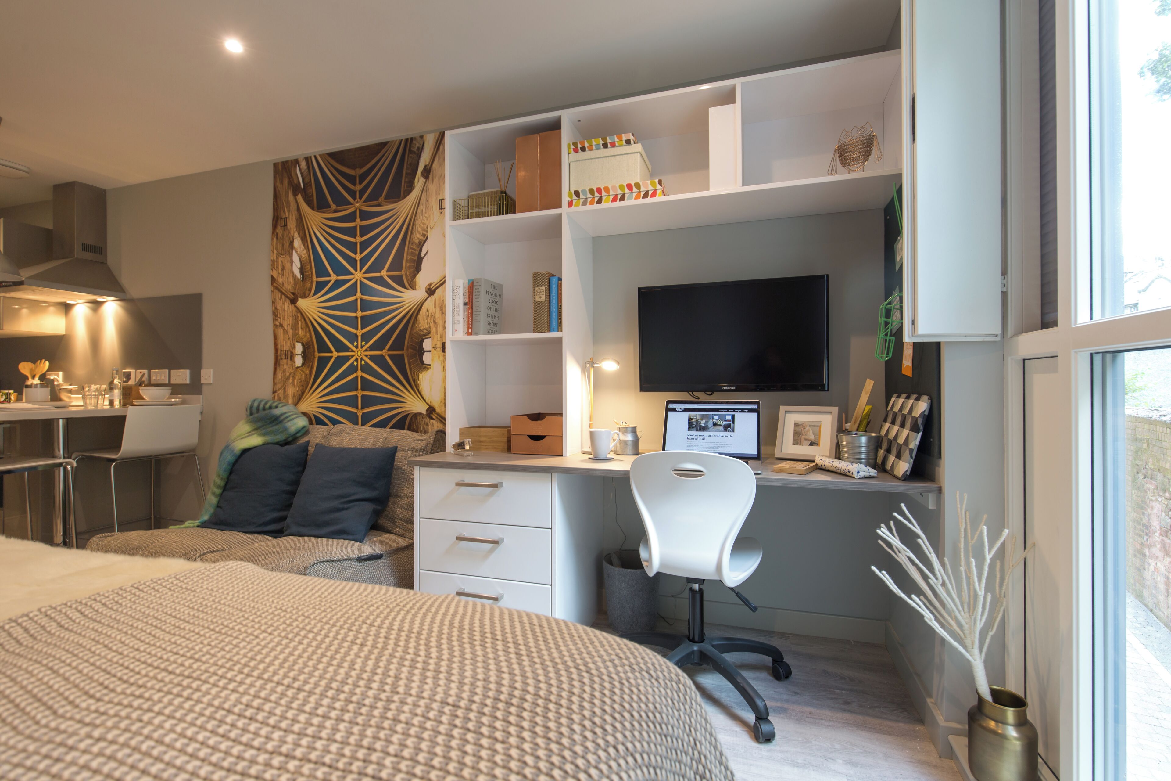 A modern bedroom with a bed, a desk, a chair, and a TV.
