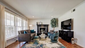 A living room with a fireplace, a television, and a large window with blinds.