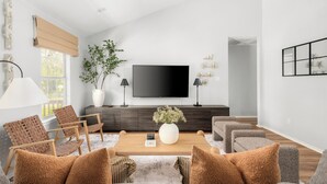 Una sala de estar moderna con un televisor de pantalla plana grande, una mesa de centro de madera y asientos cómodos.