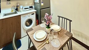 Une cuisine compacte dotée de meubles en bois, d’un lave-linge, d’un four à micro-ondes et d’un coin repas avec une table dressée pour deux personnes.