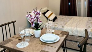 Un coin repas aménagé avec soin, avec une table dressée pour deux personnes, une orchidée en pot et, au fond, un lit agrémenté d’un coussin à rayures.