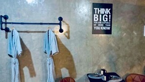 Une pièce avec un mur en béton, un portant à vêtements, deux chaises marron, une petite table avec une assiette et une tasse, et une citation inspirante sur le mur.