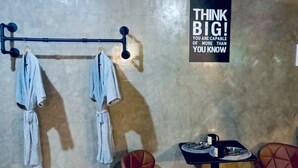 Une pièce avec un mur en béton, un portant à vêtements, deux chaises marron, une petite table avec une assiette et une tasse, et une affiche motivante.