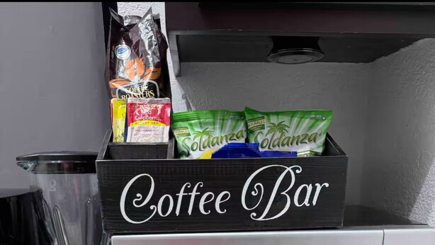 A kitchen counter with a coffee maker, a blender, a microwave, and a box labeled "Coffee Bar" containing coffee pods and a bag of coffee. - Charming 1-bedroom apartment in Montego Bay near beaches andrestaurants (Montego Bay)