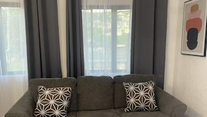 A grey sectional sofa with patterned cushions, a grey rug, and a window with grey curtains. - Charming 1-bedroom apartment in Montego Bay near beaches andrestaurants (Montego Bay)