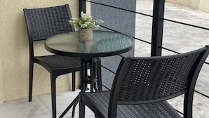 A small outdoor balcony with a glass table and two wicker chairs, a potted plant, and a doormat. - Charming 1-bedroom apartment in Montego Bay near beaches andrestaurants (Montego Bay)