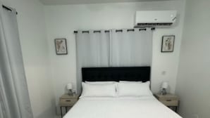 A bedroom with a large bed, two bedside tables, a ceiling fan, and an air conditioning unit. - Charming 1-bedroom apartment in Montego Bay near beaches andrestaurants (Montego Bay)