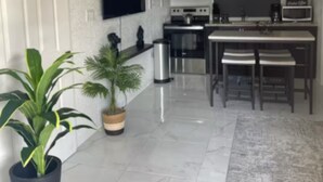 A modern kitchen with white cabinetry, a large island, and a flat-screen TV mounted on the wall. - Charming 1-bedroom apartment in Montego Bay near beaches andrestaurants (Montego Bay)