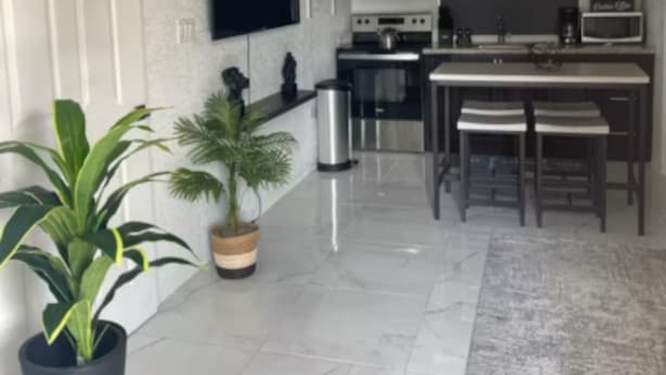 A modern kitchen with white cabinetry, a large island, and a flat-screen TV mounted on the wall. - Charming 1-bedroom apartment in Montego Bay near beaches andrestaurants (Montego Bay)
