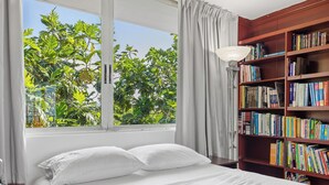 Una camera da letto con un'ampia finestra, un letto con lenzuola bianche e una libreria piena di libri.