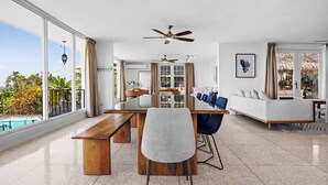 Un'ampia zona giorno con una grande finestra, un tavolo da pranzo, un divano e una ventola a soffitto.