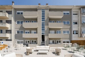 Ein mehrgeschossiges Gebäude mit einer zentralen Treppe, einer Außenbereich-Sitzgelegenheit mit Tischen und Stühlen sowie Balkonen.