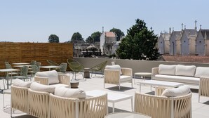 Une terrasse sur le toit aménagée avec des meubles en osier blanc, notamment des canapés et des fauteuils, ainsi qu’une table en verre.