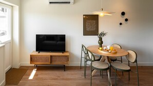 Un salon moderne avec un téléviseur à écran plat posé sur une console en bois, une table à manger avec des chaises et un luminaire suspendu.