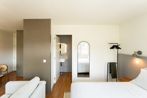 Ein Hotelzimmer mit Bett, Sessel, Nachttisch, Lampe und Spiegel.