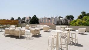 Une terrasse sur le toit, aménagée avec des espaces de détente en plein air, notamment des canapés et des tables, et offrant une vue sur les bâtiments historiques en arrière-plan.