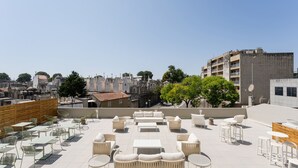 A rooftop terrace with outdoor seating, including sofas and tables, overlooking a cityscape with buildings and trees.