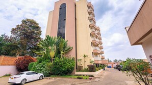 A multi-story hotel with a central tower, balconies, and a parking area with a white car.