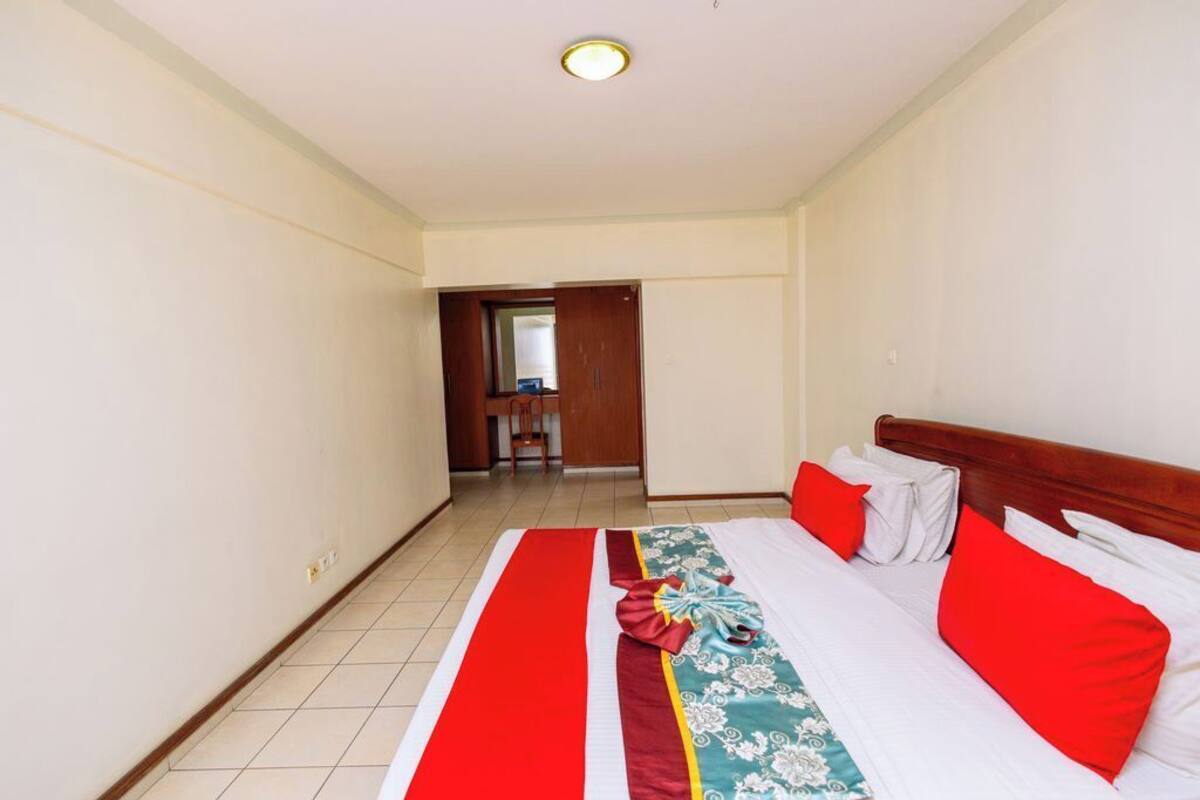 A hotel room with a large bed, red and white bedding, a wooden headboard, and a tiled floor.